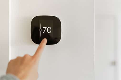 A person adjusting the thermostat on the wall of their home