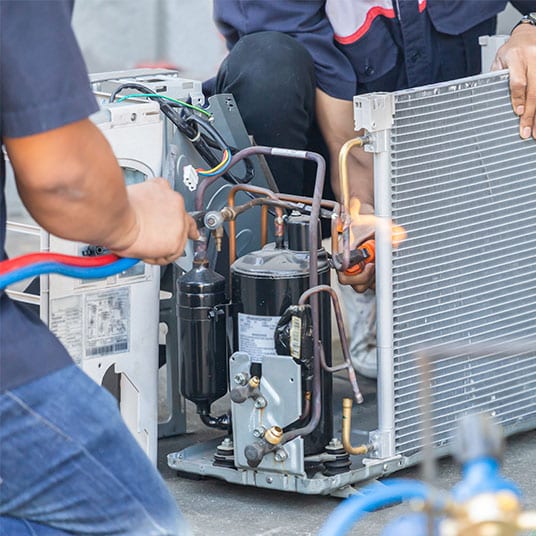Two HVAC technicians working on an outside air conditioner unit