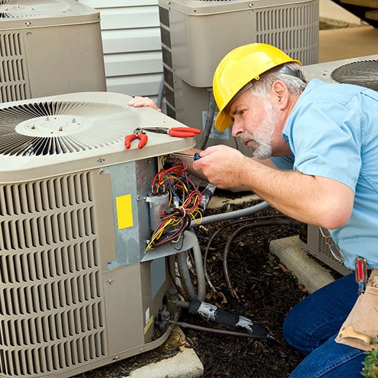 A residential HVAC technician performing regular maintenance on an air conditioning condenser outside a house